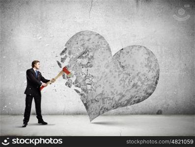 Determined businessman. Young businessman breaking stone heart with axe