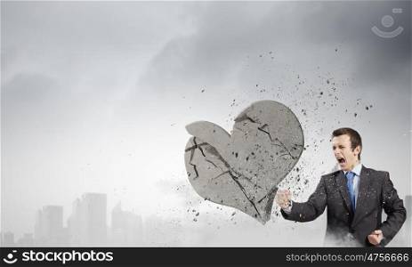 Determined businessman. Young businessman breaking stone heart with punch