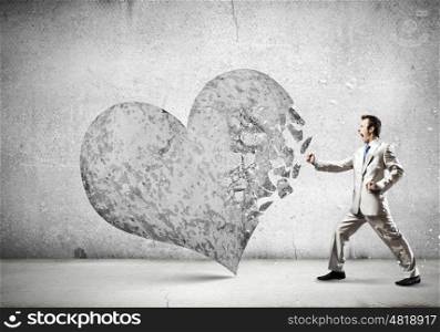 Determined businessman. Young businessman breaking stone heart with punch