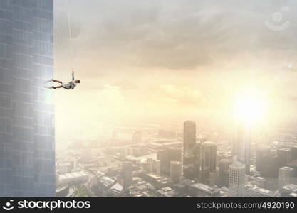 Determined businesswoman climbing building with help of rope. Getting to top