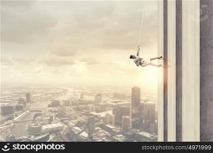Determined businesswoman climbing building with help of rope. Getting to top