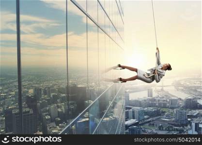 Determined businesswoman climbing building with help of rope. Getting to top
