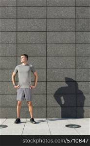 Determined jogger standing with hands on hips against tiled wall outdoors