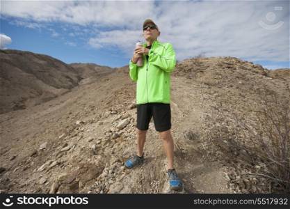 Determined senior man holding water bottle while standing on mountain