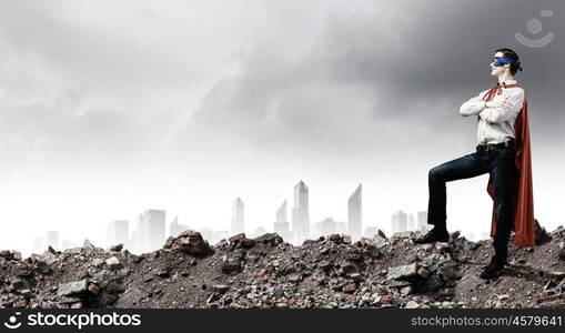 Determined superman. Confident superman in cape and mask standing on ruins