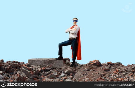 Determined superman. Confident superman in cape and mask standing on ruins