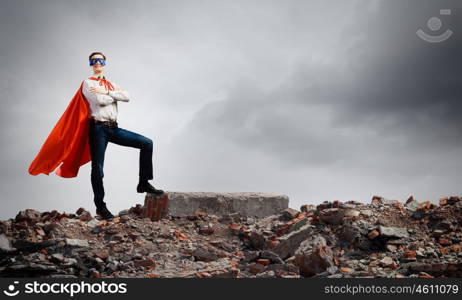 Determined superman. Confident superman in cape and mask standing on ruins