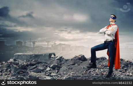 Determined superman. Confident superman in cape and mask standing on ruins