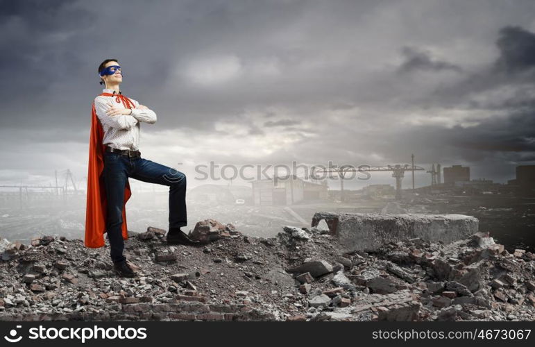 Determined superman. Confident superman in cape and mask standing on ruins