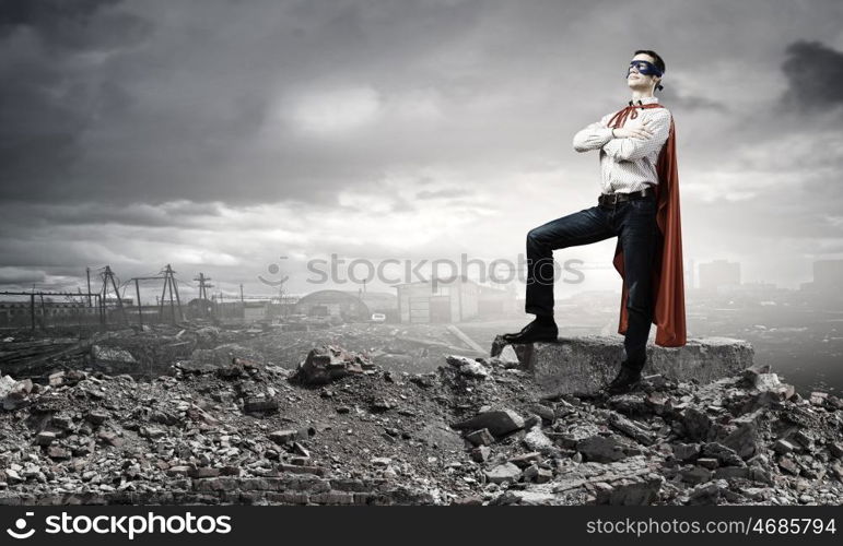 Determined superman. Confident superman in cape and mask standing on ruins