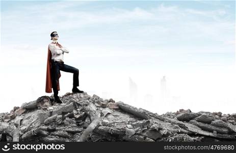 Determined superman. Confident superman in cape and mask standing on ruins