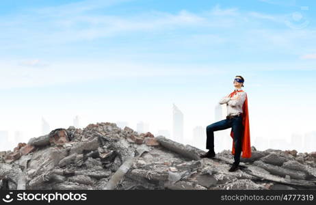 Determined superman. Confident superman in cape and mask standing on ruins