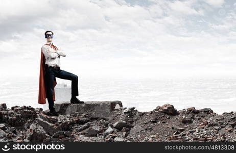 Determined superman. Confident superman in cape and mask standing on ruins