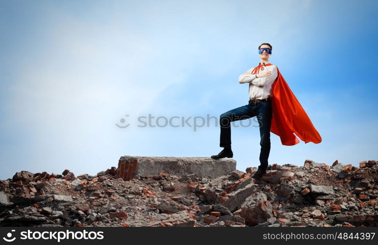 Determined superman. Confident superman in cape and mask standing on ruins