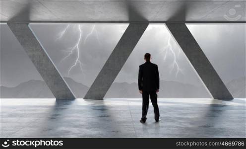 Determined to face difficulties. Back view of businessman looking at lightning through office window
