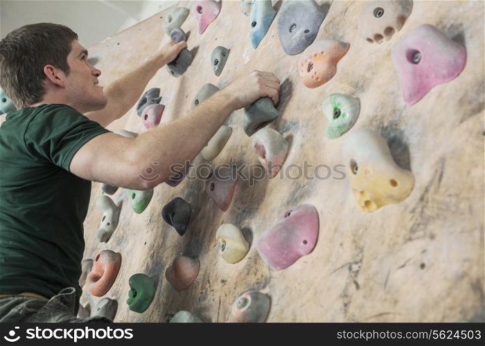 Determined young man climbing up a climbing wall in an indoor climbing gym, low angle view