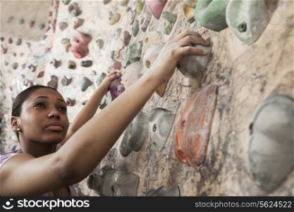 Determined young woman climbing up a climbing wall in an indoor climbing gym