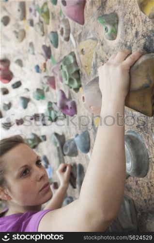 Determined young woman climbing up a climbing wall in an indoor climbing gym
