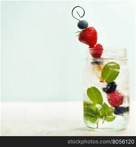 Detox fruit infused flavored water. Refreshing summer homemade cocktail. Fresh summer fruits on metal stick.