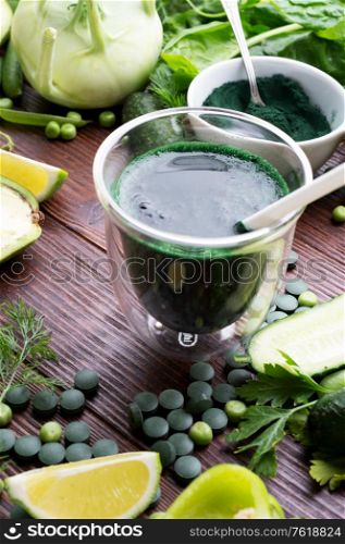 detox green cocktail with spirulina around vegetables. lifestyle concept. various fresh green vegetables at wooden table.