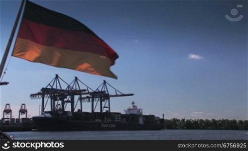 Deutschlandflagge vor blauem Himmel, im Hintergrund KrSne und Containerschiff.
