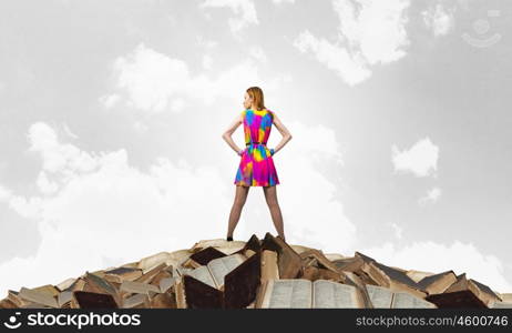 Develop your imagination. Woman in multicolored dress standing on pile of books