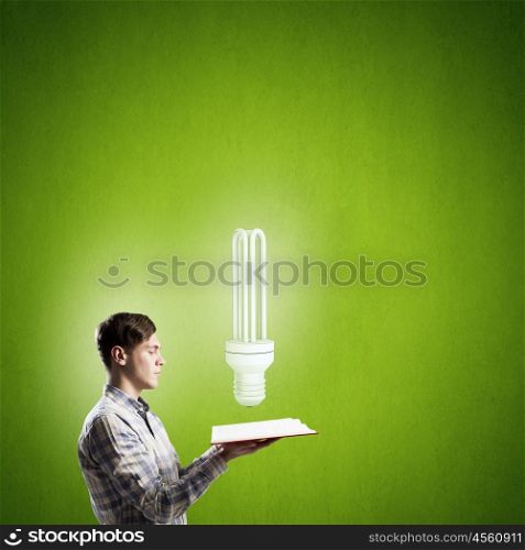 Develope your mind and creativity. Young man with opened book and bulb on it on color background