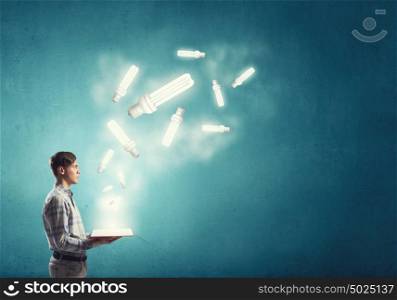 Develope your mind and creativity. Young man with opened book and bulb on it on color background