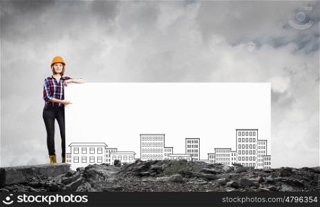 Development project. Young woman builder wearing helmet and holding banner with construction sketches