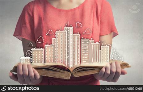 Development project. Young woman in red dress holding opened book with city model