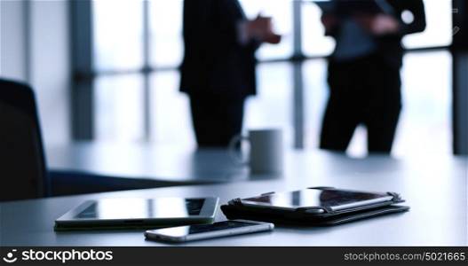Devices on table with business people in background in modern office building