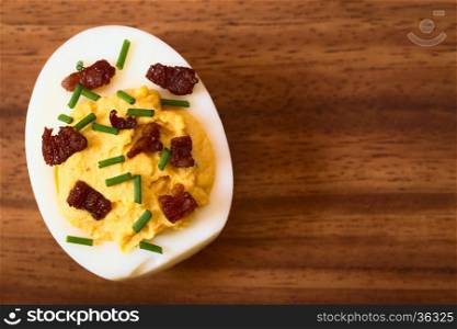 Deviled egg with bacon and chives, photographed overhead on wooden plate with natural light (Selective Focus, Focus on the top of the egg yolk)