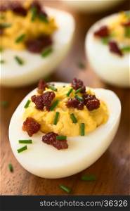 Deviled egg with bacon and chives, photographed with natural light (Selective Focus, Focus on the front of the egg yolk of the first egg)
