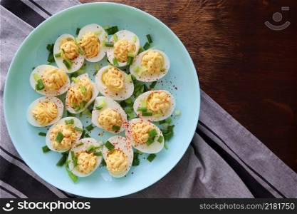 Deviled Eggs sprinkled with paprika and chopped green onion on a green plate on a woodene table . Top view .. Deviled Eggs sprinkled with paprika and chopped green onion on a green plate on a woodene table . Top view