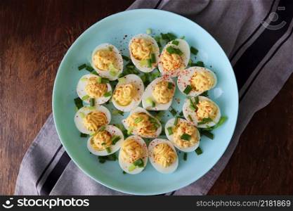 Deviled Eggs sprinkled with paprika and chopped green onion on a green plate on a woodene table . Top view .. Deviled Eggs sprinkled with paprika and chopped green onion on a green plate on a woodene table . Top view