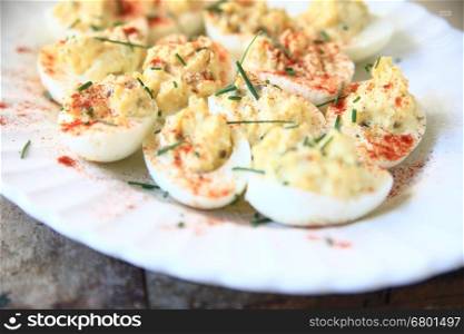 Deviled eggs with smoked paprika and chives on a white fluted platter