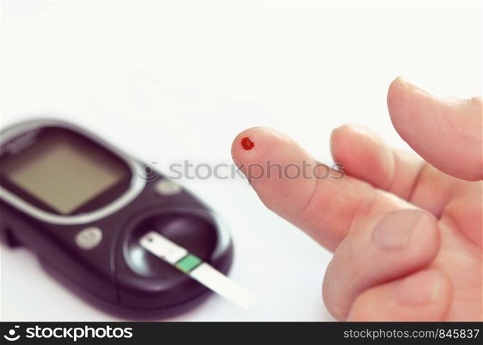 Diabetes health care concept - close up of senior man hands checking blood sugar level by glucometer.