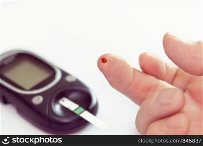 Diabetes health care concept - close up of senior man hands checking blood sugar level by glucometer.