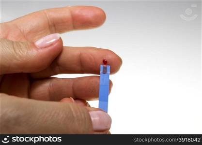 Diabetic places a drop of blood on a test strip.You see a drop of blood on a finger and measuring bar.Close.Vertical view