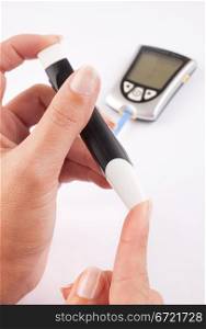 Diabetic woman pricking her finger for a blood test with a glucometer in the background