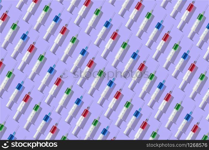 Diagonal medical pattern from plastic disposable syrenges with red, blue and green liquid on a pastel lavender background. Flat lay.. Health-care pattern from colorful vaccine&rsquo;s plastic syrenges.