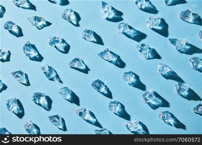 Diagonal rows of transparent pieces of glass ice on a blue background, food pattern with top view. Pattern of pieces of clear glass ice on a blue background