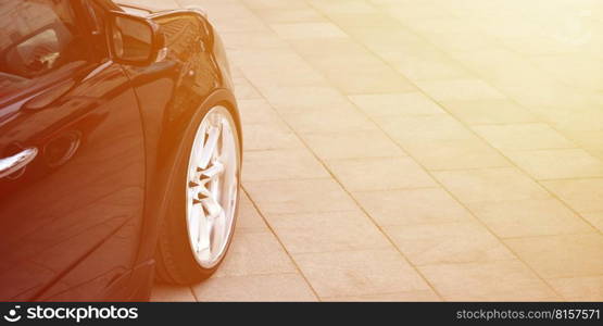 Diagonal view of a black glossy car with white wheels, which stands on a square of gray tiles