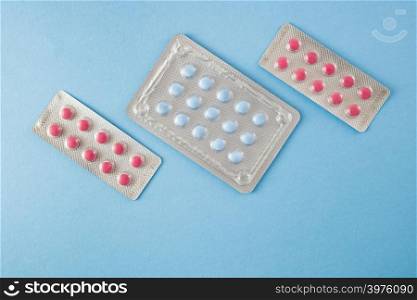 Diagonally arranged blister packs of blue and pink pills on blue background- healthcare and medical concept