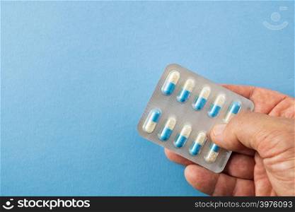 Diagonally arranged hand holding a blister pack of blue and white pills on blue background with copyspace- healthcare and medical concept