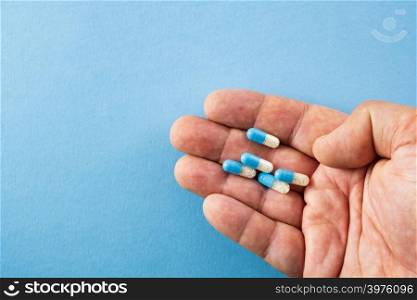 Diagonally arranged hand holding blue and white pills on blue background with copyspace- healthcare and medical concept