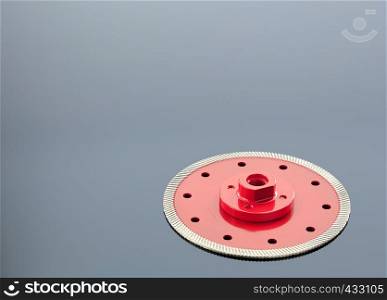 Diamond cutting wheel is red with a threaded nut, on the left side is a copy space on the mirror surface of a gray background with a slight gradient.. Diamond cutting wheel is red with a threaded nut on the mirror surface of a gray background with a slight gradient