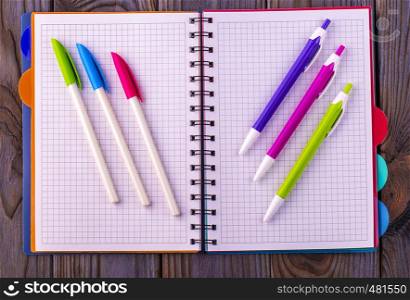 Diary (notebook) and colored pens on wooden background.