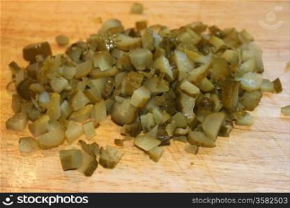 Diced green pickles on a wooden board.