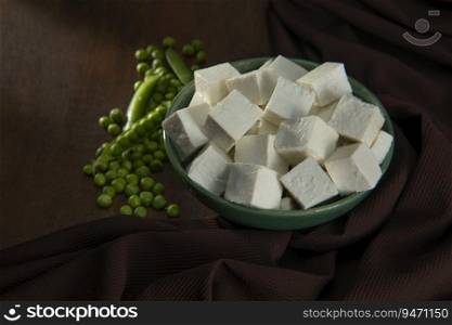 Diced Paneer in a green bowl with fresh raw peas 